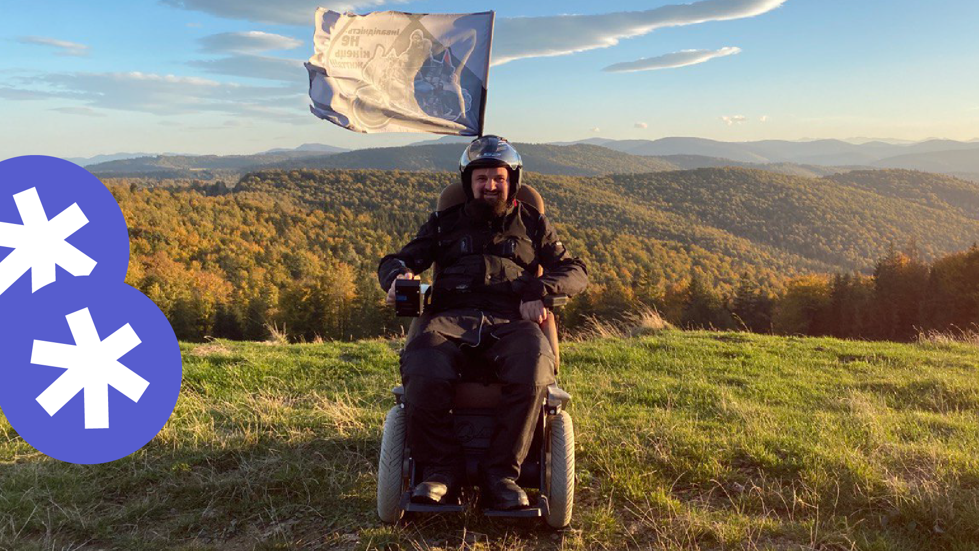 Чоловік, який користується кріслом колісним знаходиться на горі. До крісла колісного прикріплений прапор із написом "інвалідність не кінець життя"