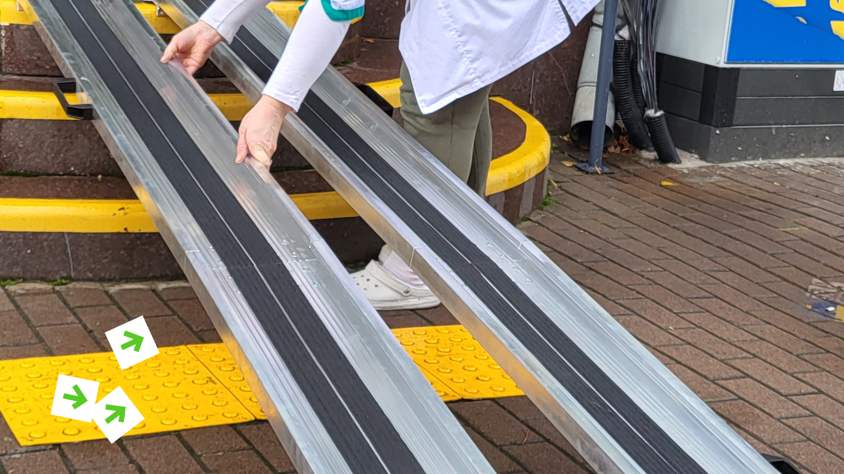 Опис зображення: на фото сходинки, які ведуть до приміщення. На цих сходинках людина розкладає апарелі — це дві залізні рейки.