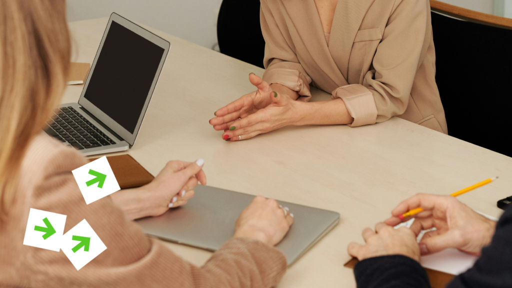 Фрагмент фото, на якому троє людей сидять за столом. У кадрі один закритий і один відкритий ноутбук.